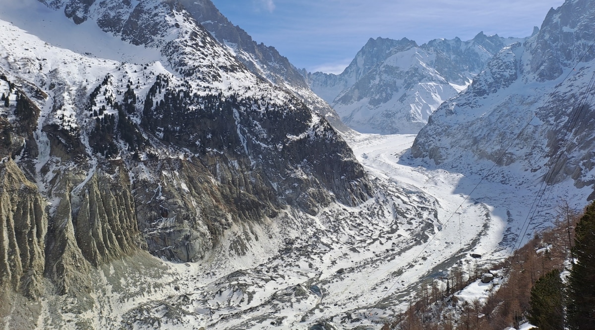 landscape of Mer de Glace, nestled in the Chamonix Valley of the French Alps. Towering ice cliffs dominate the scene. The glacier's vast expanse stretches between dramatic mountain peaks, forming a frozen river of ice that winds its way through the rugged terrain.