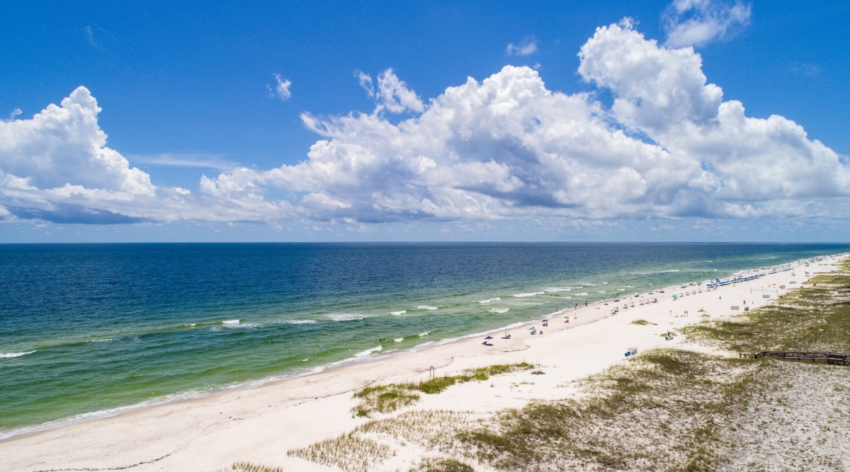 A photograph showcasing Mickler Beach in St. Augustine, Florida. The image captures the beach's sandy shoreline against the backdrop of the Atlantic Ocean. Sunbathers and beachgoers are visible. The scene depicts the typical coastal landscape of St. Augustine, featuring a wide stretch of sand and a calm ocean horizon.
