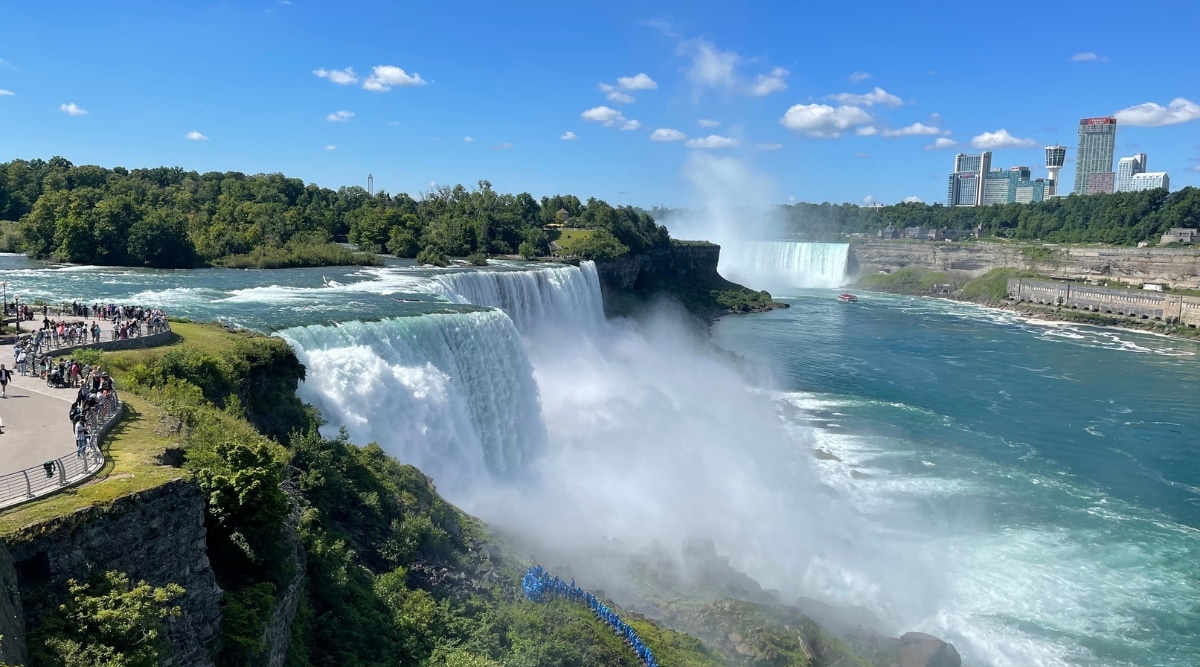 A photograph capturing Niagara Falls, situated on the border of New York and Ontario. The image showcases the iconic waterfall surrounded by natural rock formations. The Falls are framed by the urban landscapes of Niagara Falls, New York, and Ontario. Visitors can be seen observing the Falls from designated viewpoints.
