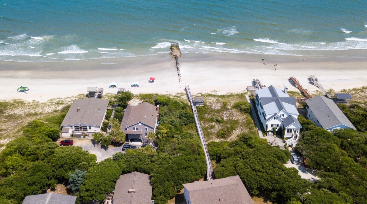A photograph capturing Porpoise Point in St. Augustine, Florida. The image presents the coastal area with a focus on the shoreline and the adjacent waters. There are several houses and a green area in front of the beach.