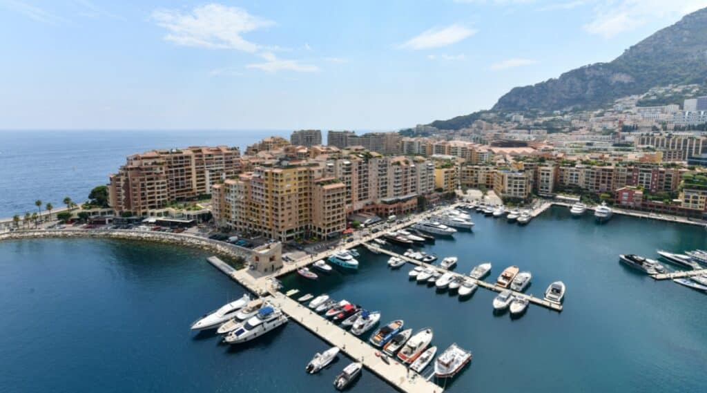 Port de Fontvieille in Monaco. The image showcases the marina with a collection of luxurious yachts and sailboats, set against the azure waters of the Mediterranean Sea. The facades of elegant waterfront buildings surround the port, reflecting a blend of modern architecture and coastal charm.