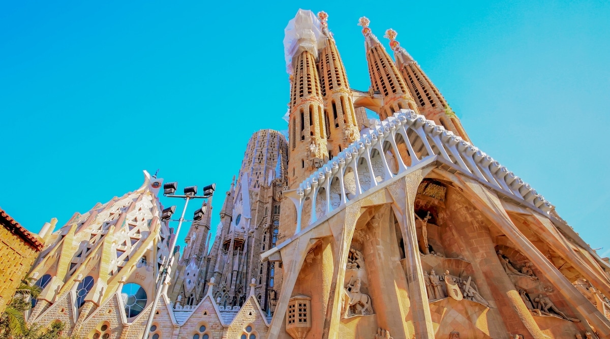 Sagrada Familia in Barcelona, Spain. The Sagrada Familia's facades are adorned with intricate sculptures and intricate religious iconography, depicting scenes from the Bible. Towering spires rise against the vibrant blue sky, creating a harmonious interplay of divine design and natural beauty. 