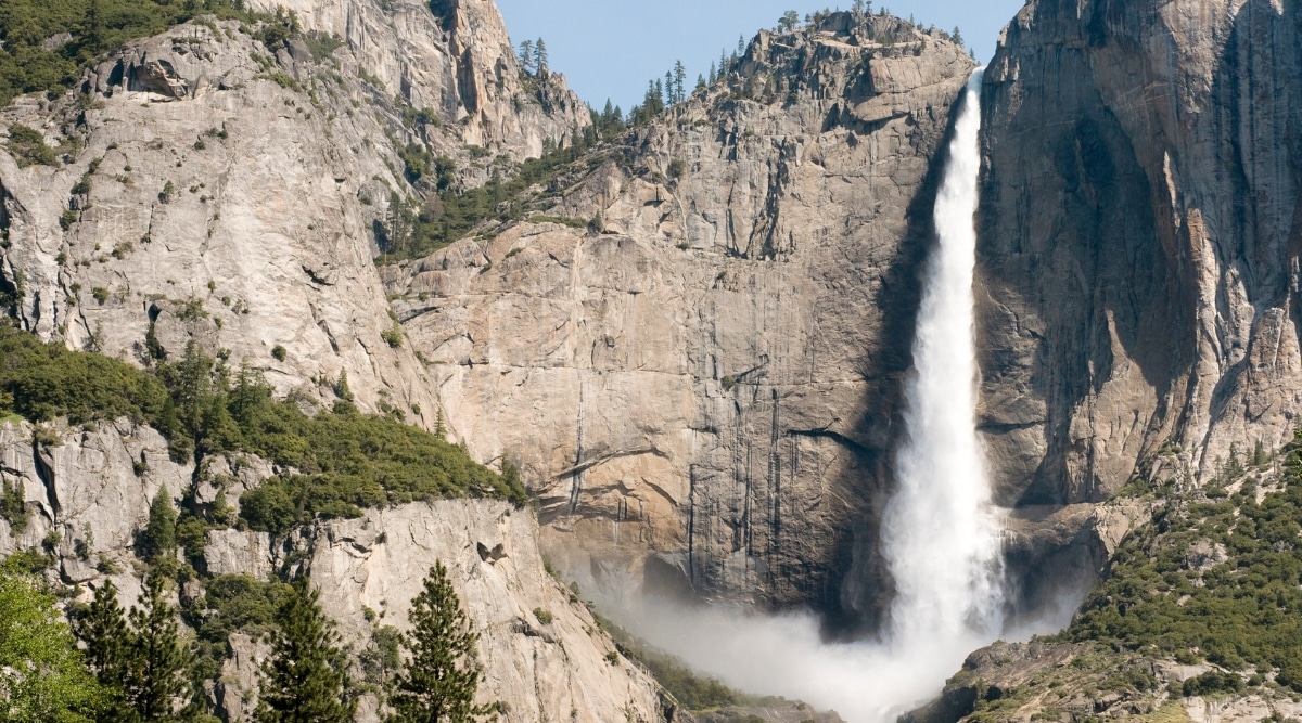 A photograph capturing Upper Yosemite Falls in California. The image displays the iconic waterfall against a backdrop of granite cliffs and lush greenery. Water cascades down the rocky terrain.