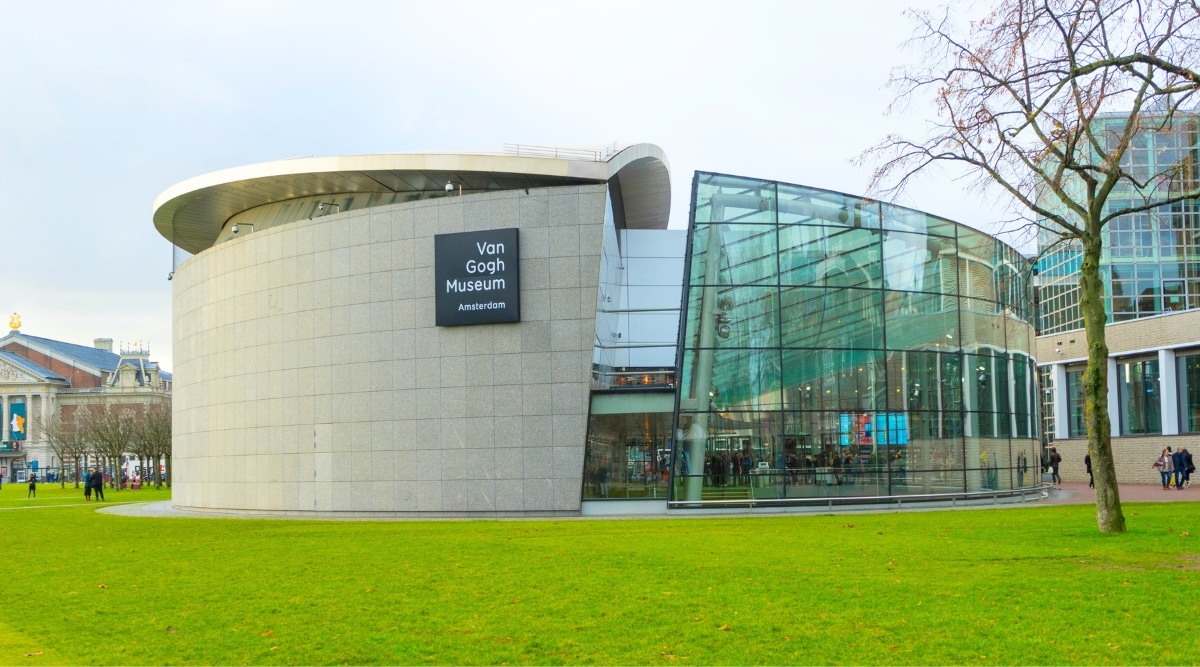 Photograph capturing the grandeur of the Van Gogh Museum in Amsterdam. The image showcases the museum's modern architectural design, with sleek lines and large glass panels inviting natural light into the gallery spaces. The vibrant outdoor surroundings, including lush greenery.