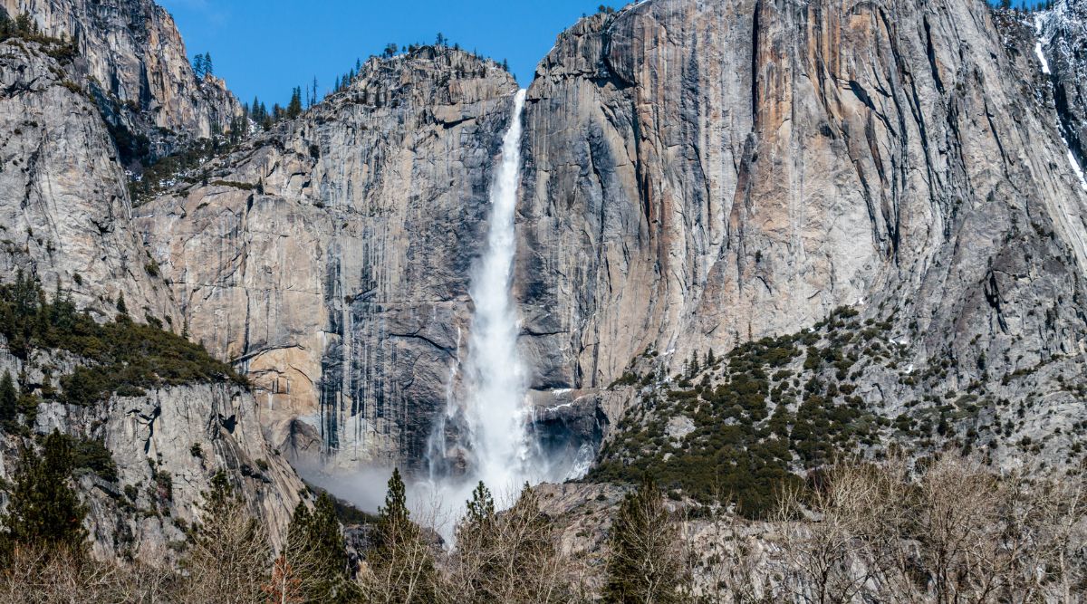 A photograph capturing Yosemite Falls in California. The image showcases the iconic waterfall within Yosemite National Park against a backdrop of granite cliffs. The falls cascade in a series of stages.