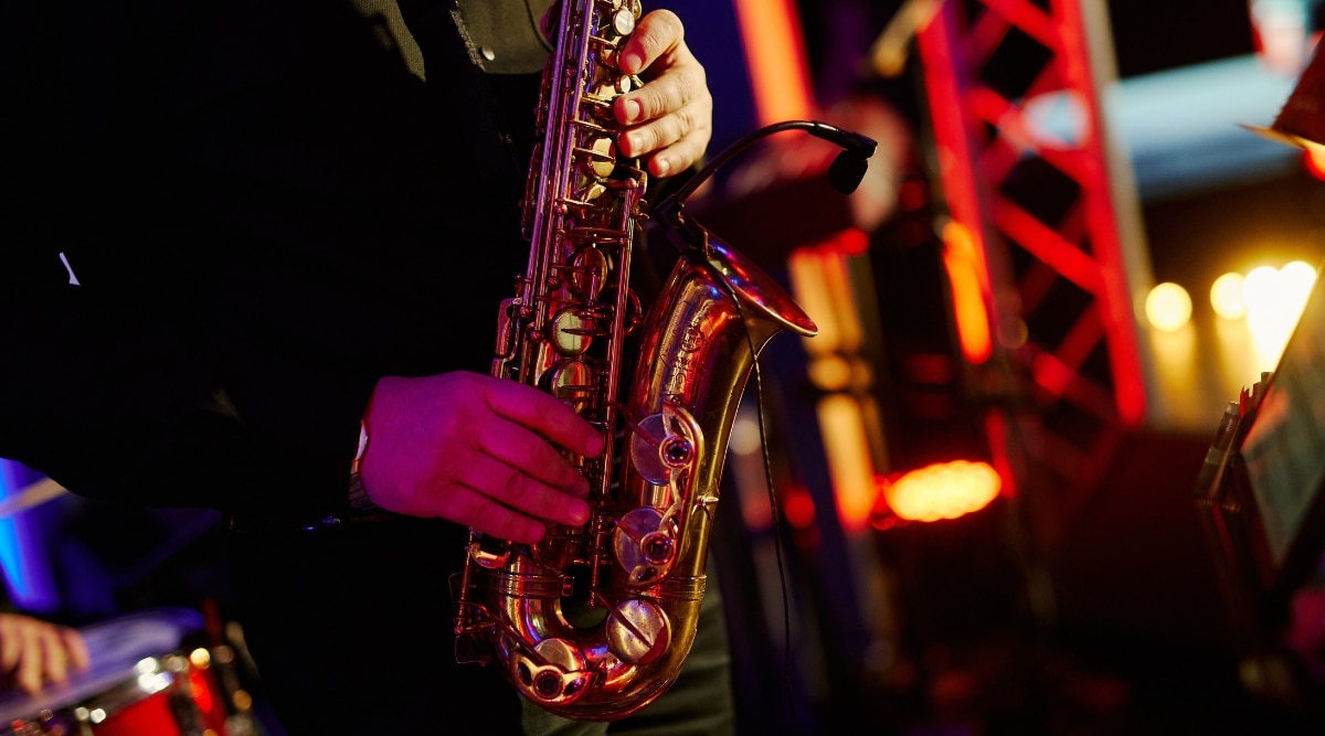 Close-up of a musician playing the saxophone in a bar. The musician is wearing a black shirt and has a gold watch on his right wrist. The saxophone is a distinctive musical instrument with a sleek and curvaceous design.