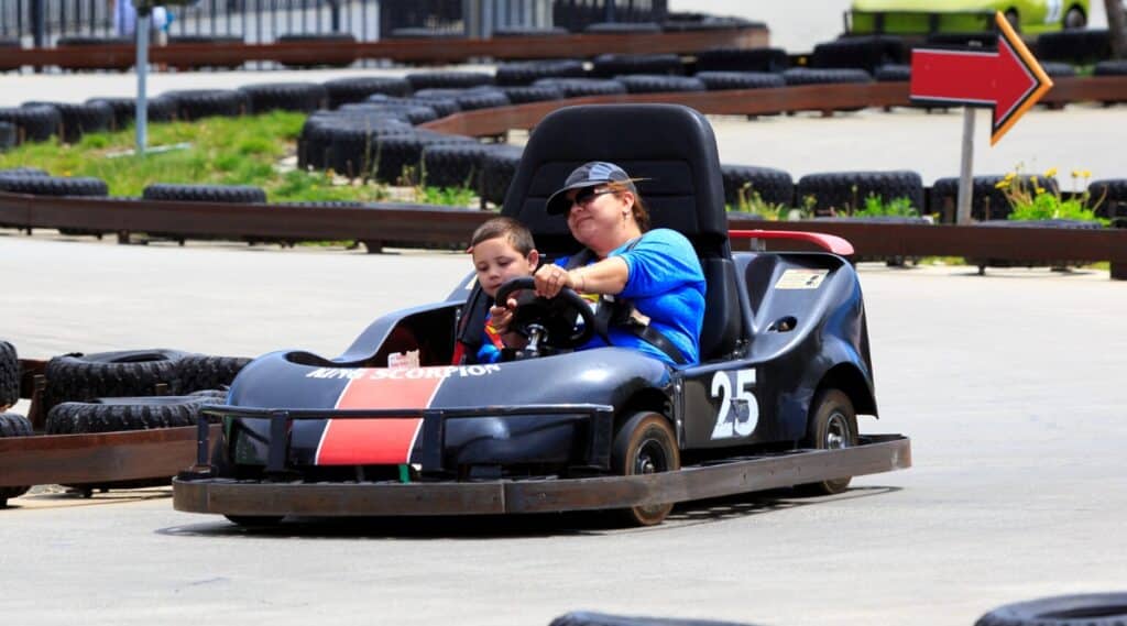 racing track. Close-up of mother and child in black Go-kart. Go-kart is a small, open-wheel vehicle designed for racing on kart tracks. The woman and child are wearing blue T-shirts with the Superman logo.
