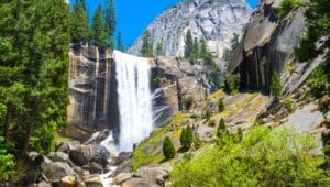 A photograph featuring Vernal Fall in California. The image captures the waterfall amidst the surrounding natural landscape. The cascading water descends from a significant height, creating a visually striking element within the scenery.