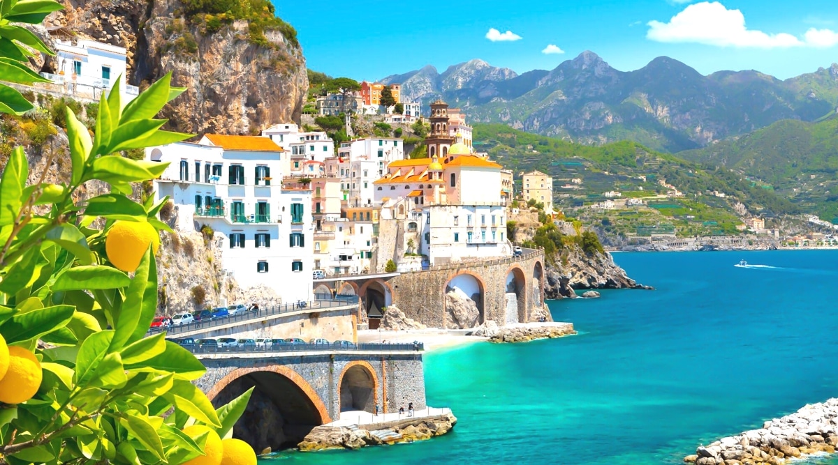 A photograph capturing the coastal town of Amalfi, Italy. The image showcases the urban setting against the backdrop of the Tyrrhenian Sea. The town's architecture, characterized by colorful buildings, is visible along the waterfront. There are a lot of mountains in the background.