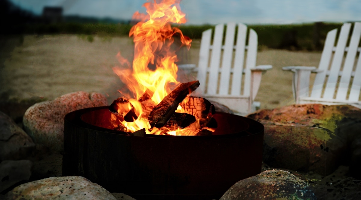A photograph depicting a close-up view of a bonfire on a beach in Los Angeles, California. The image captures the flames with a backdrop of several white wooden seats in the background.
