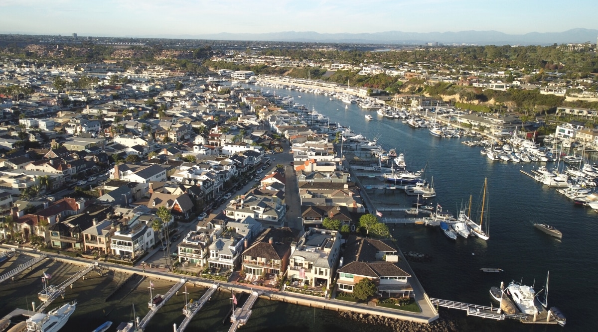 An aerial view capturing Balboa Island and Newport Harbor in Newport Beach, California. The image provides a comprehensive perspective of the coastal landscape, featuring the island and harbor surrounded by water.
