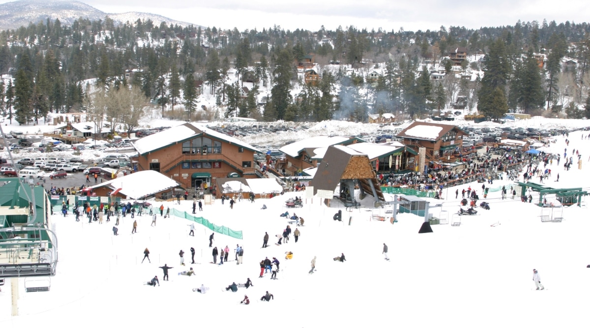 A top-down photograph depicting the winter landscape of Big Bear Resort ski resort in California. The image showcases extensive snow coverage surrounding the resort, with visitors engaged in winter recreational activities.