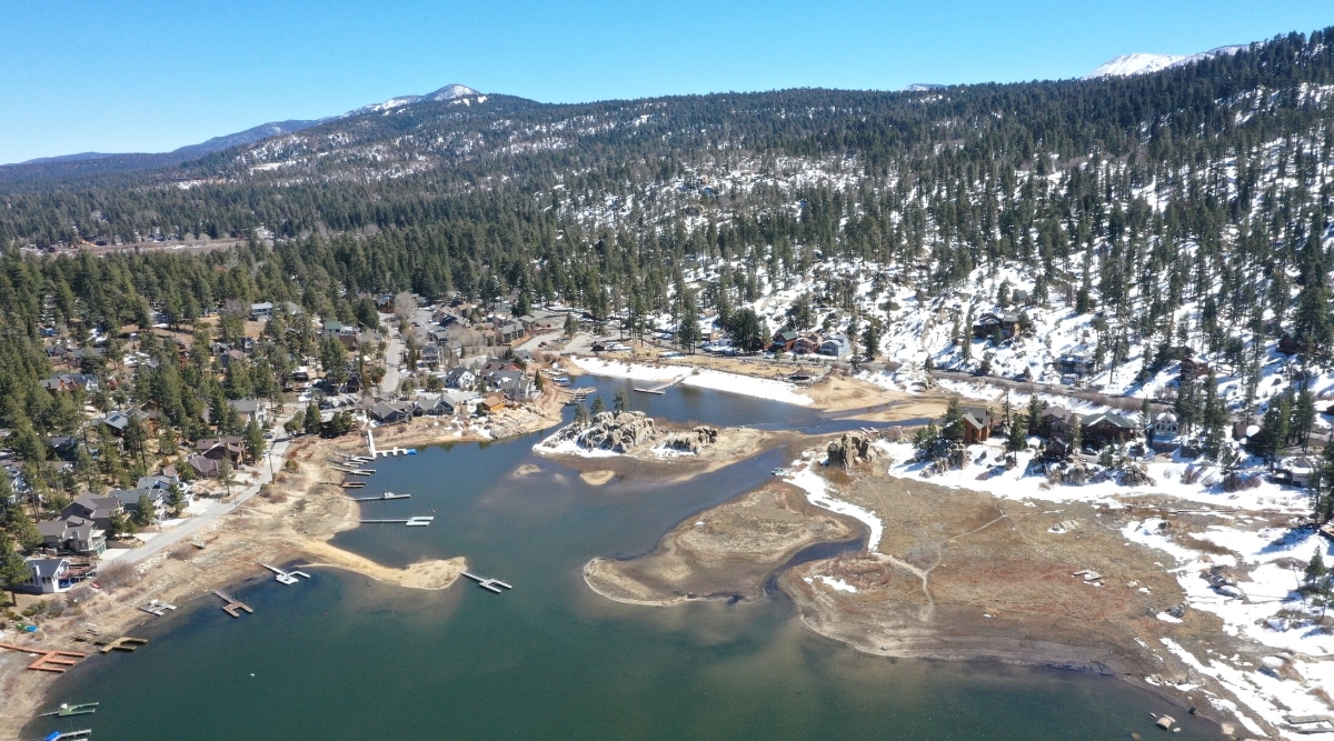 A top view capturing Big Bear Lake in California. The image showcases the lake's expansive surface area surrounded by wooded landscapes and mountainous terrain. The surrounding environment consists of dense forested areas and occasional clearings.