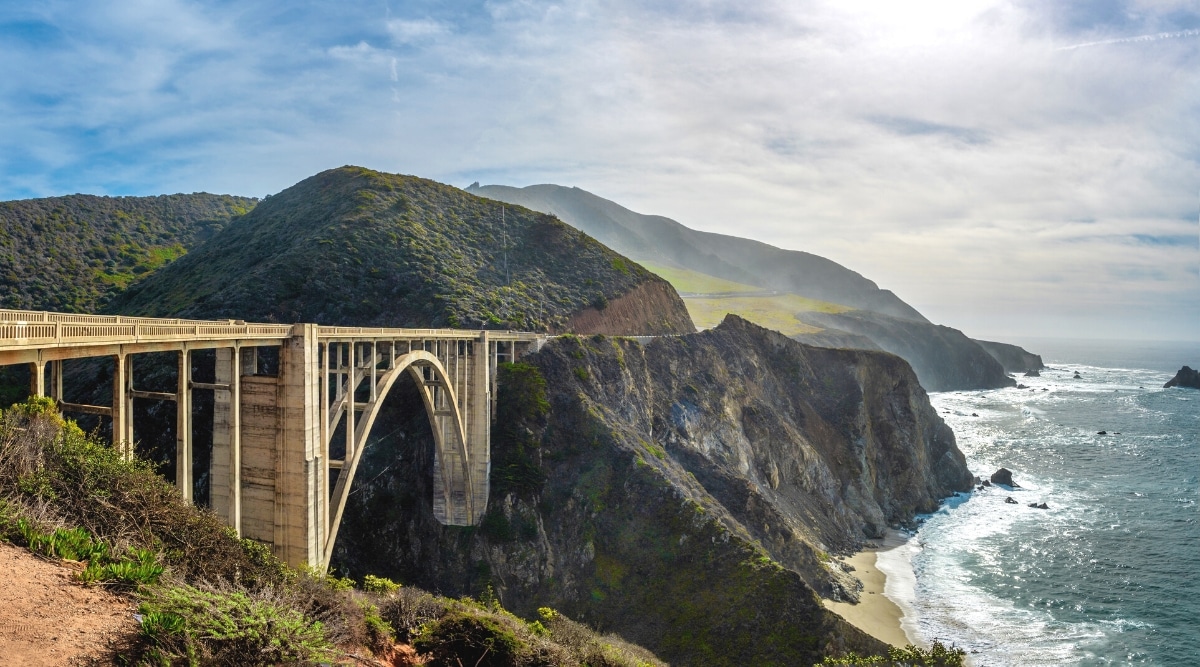The photograph depicts Bixby Bridge, an old wooden bridge with an arch, located in the Big Sur area. The image showcases the bridge's architectural features, emphasizing its arch design and wooden construction.