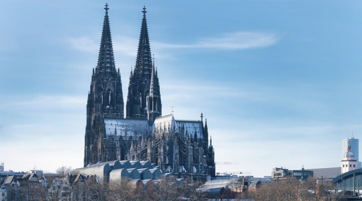 A winter cityscape featuring the Cologne Cathedral amid a snowy backdrop. The image captures the iconic cathedral's towering spires and intricate architecture against a serene, snow-covered urban environment. 