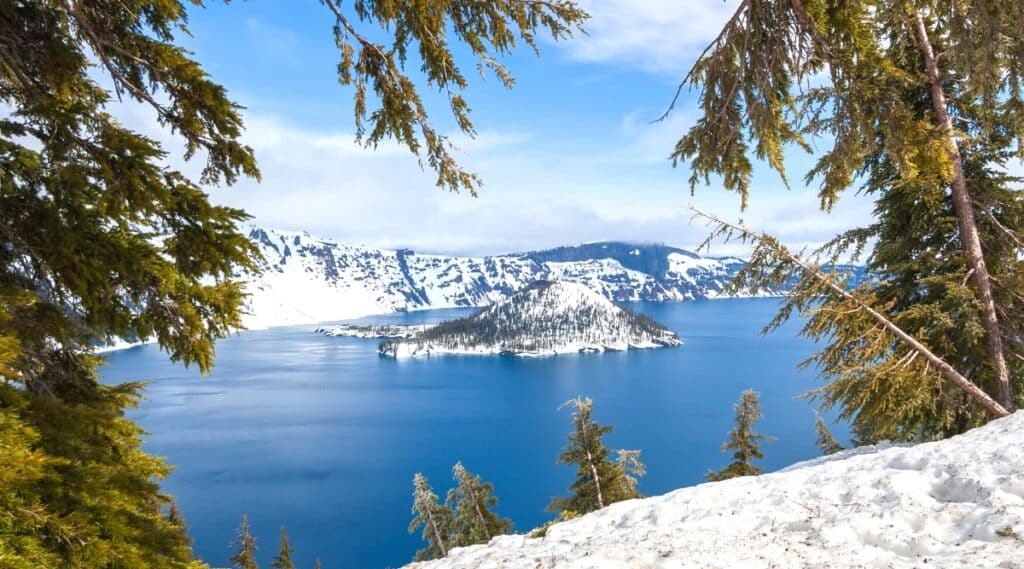 A scenic view capturing a snow-covered hill within Crater Lake National Park. The image illustrates the winter landscape with a layer of snow blanketing the hillside. The neutral sky in the background adds to the overall winter ambiance.