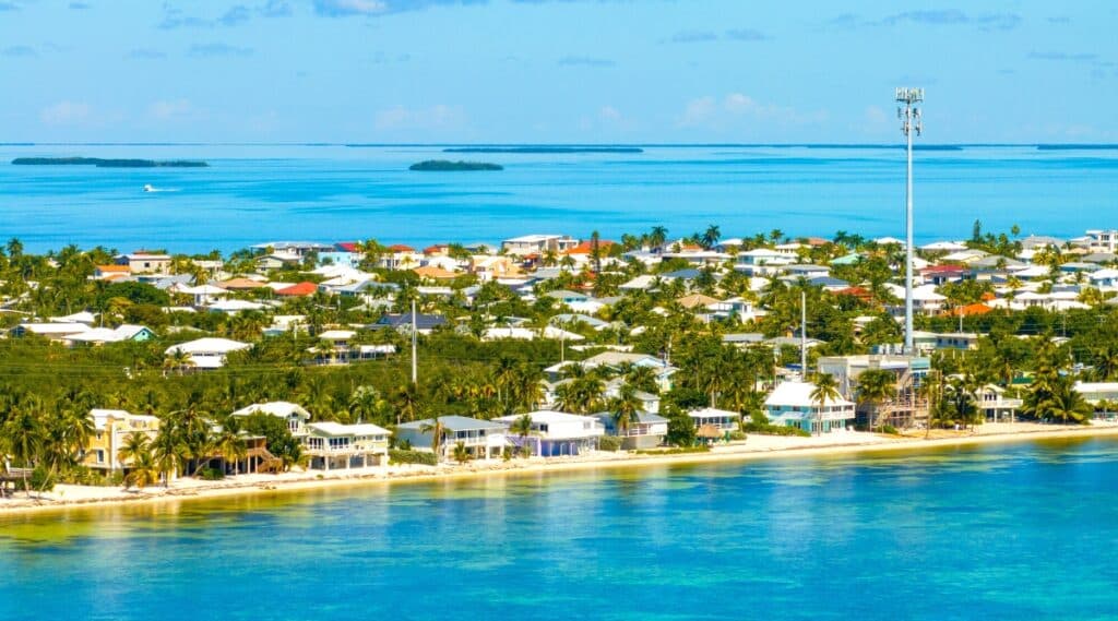 A panoramic view capturing the Florida Keys from an angled perspective. The image showcases beaches, houses, and an abundance of trees. In the background, the ocean stretches with small islands visible on the horizon.