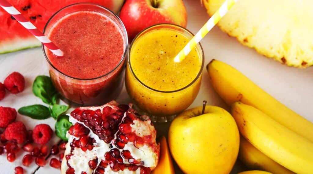 A visually appealing photograph featuring a fresh organic red and yellow smoothie. The smoothie is composed of a blend of fruits, including apple, watermelon, pomegranate, raspberry, pineapple, banana, and mango.