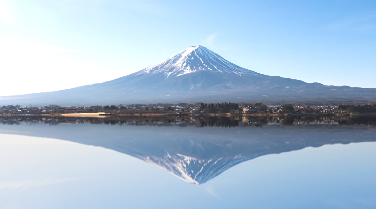 A photograph capturing Mount Fuji, or Fujisan, in its natural setting. The image showcases the iconic conical shape of the mountain, framed against a clear sky.The scene offers a straightforward representation of Mount Fuji, highlighting its distinctive silhouette and geographical prominence.