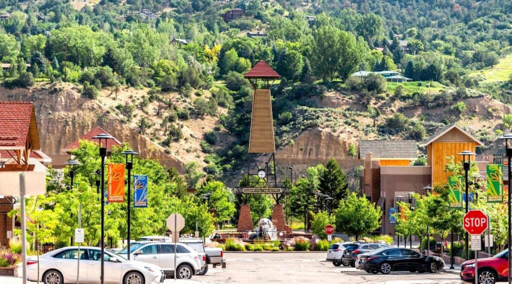 A depiction of the shopping meadows, mall, park, buildings, and parked cars in Glenwood Springs, Colorado. The image captures the commercial and recreational aspects of the town, with a particular focus on the shopping meadows. 