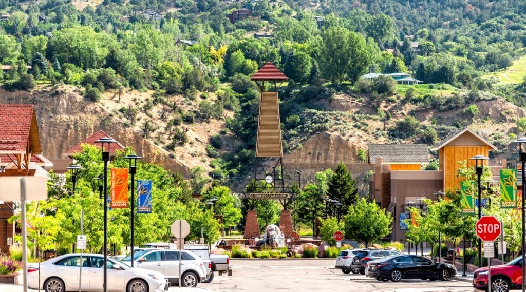A depiction of the shopping meadows, mall, park, buildings, and parked cars in Glenwood Springs, Colorado. The image captures the commercial and recreational aspects of the town, with a particular focus on the shopping meadows.