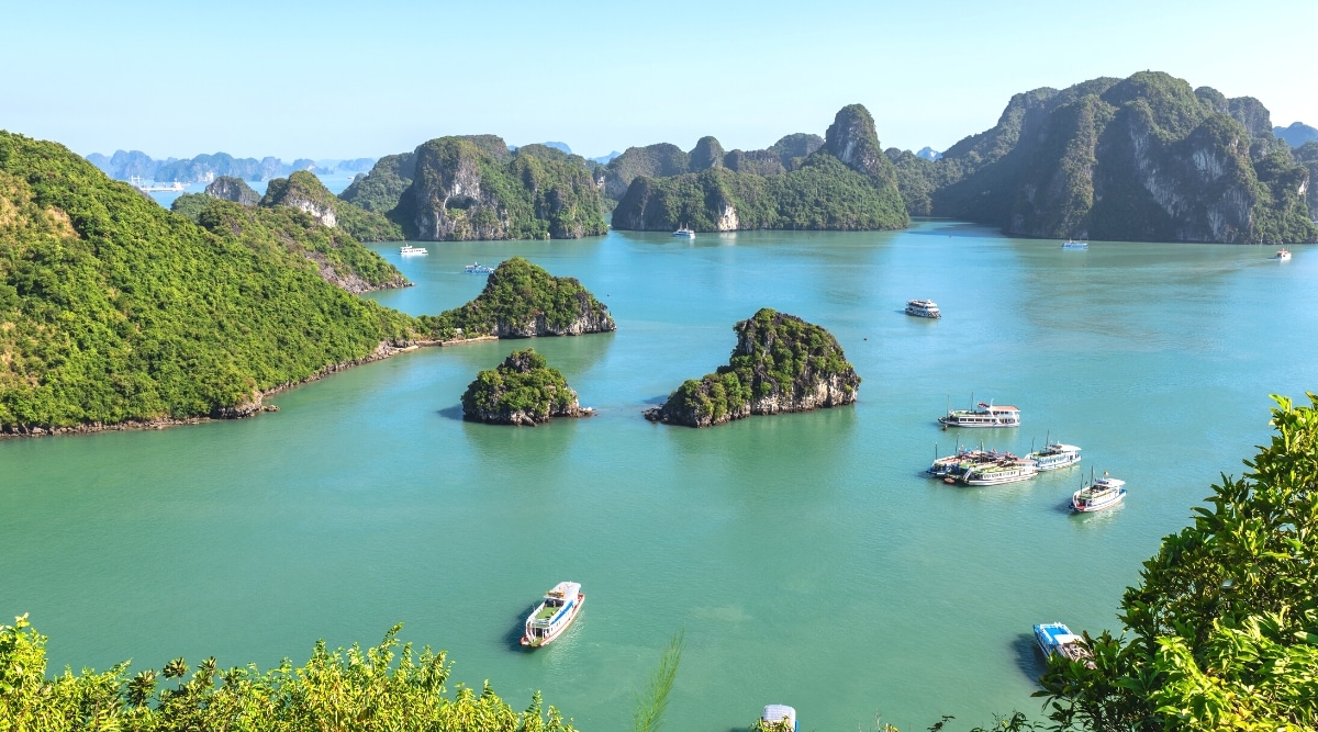 An aerial view capturing Ha Long Bay in Vietnam. The image showcases the bay's distinctive karst limestone formations, extending across the water. The atmospheric conditions are clear. Several boats can be observed navigating the bay.