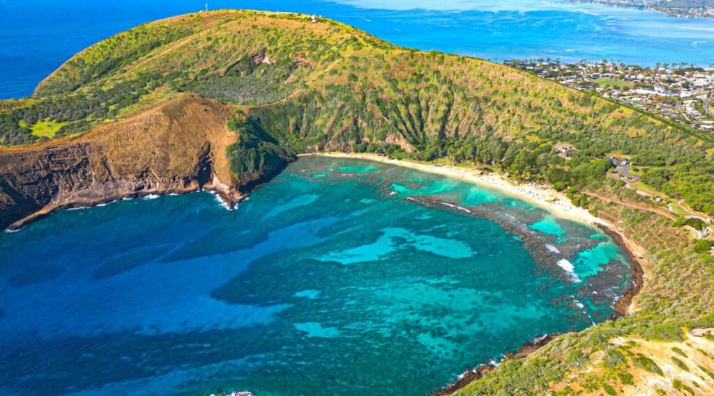 An aerial view showcasing Hanauma Bay on the island of O'ahu in Hawaii. The image provides a comprehensive overview of the bay's distinctive horseshoe shape and surrounding coastal features. The turquoise waters are visible.