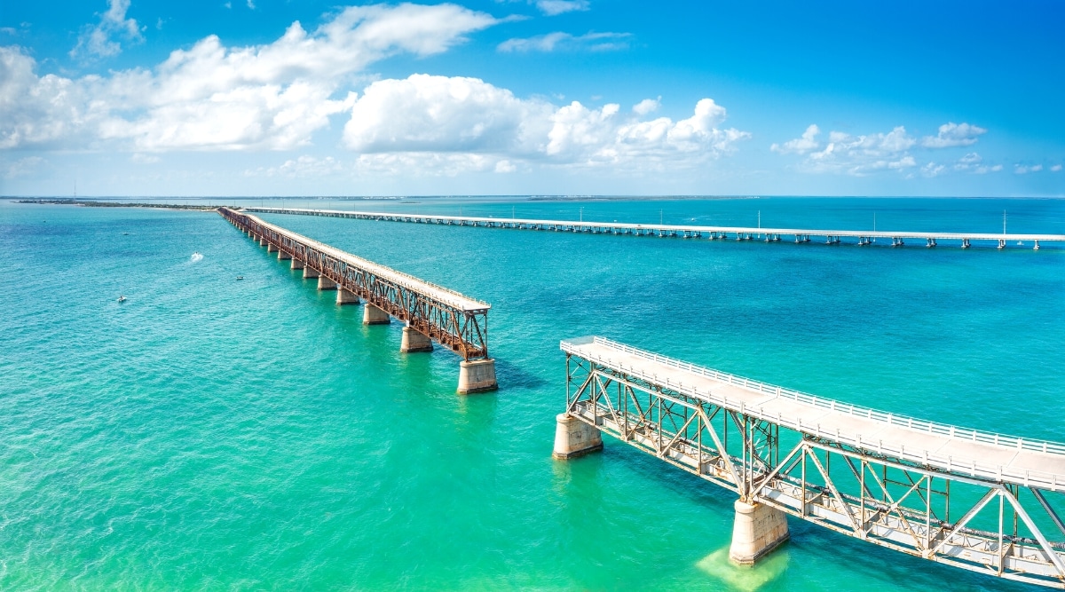 An aerial view captures the Bahia Honda Rail Bridge on a sunny day. The derelict railroad bridge spans across the lower Florida Keys, connecting Bahia Honda Key with Spanish Harbor Key. The image portrays the structural elements of the bridge.