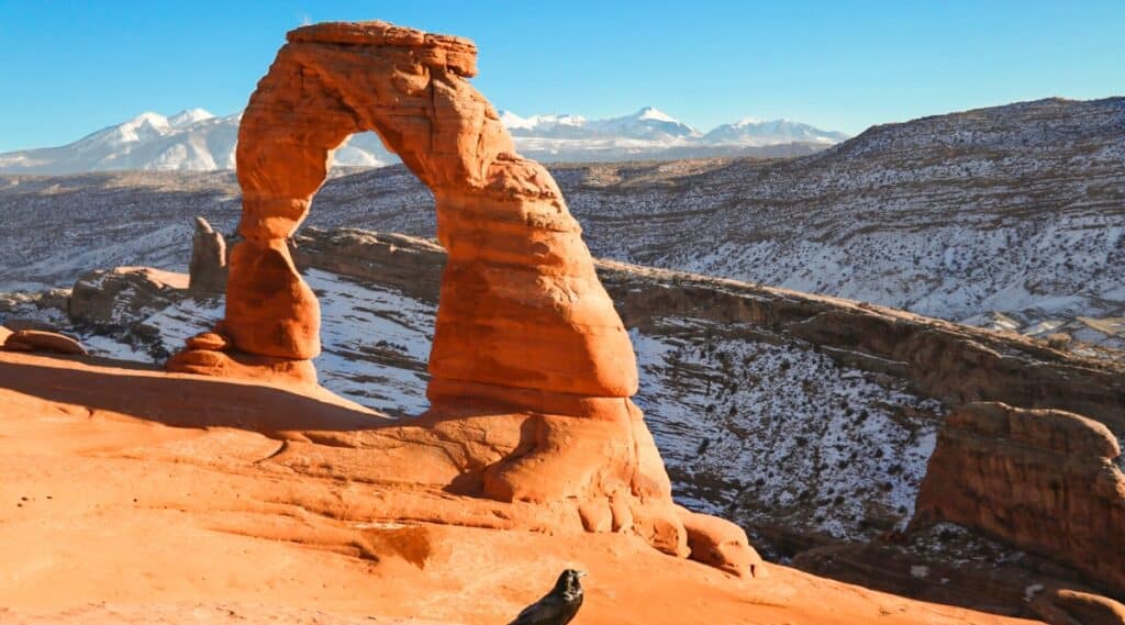 The photograph captures the 52-foot-tall Delicate Arch, a free-standing natural rock arch located in Arches National Park. This well-known natural landmark stands prominently against the backdrop of the La Sal mountain range. The image provides a clear representation of the arch's delicate and distinct form, showcasing its natural features and geographical context.