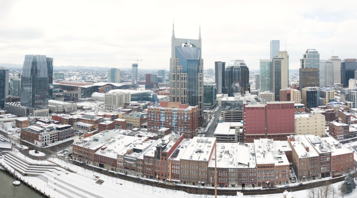 A view capturing Nashville, Tennessee. The image portrays the cityscape featuring buildings, urban infrastructure, and the flowing river. 