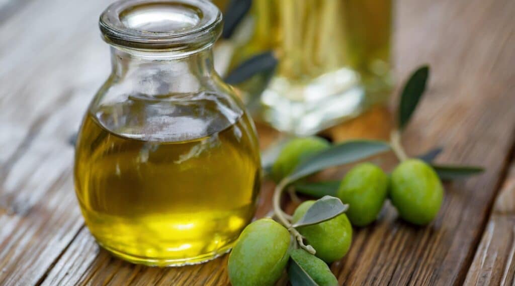 A photograph featuring two jars of olive oil placed on a wooden table alongside an olive branch.