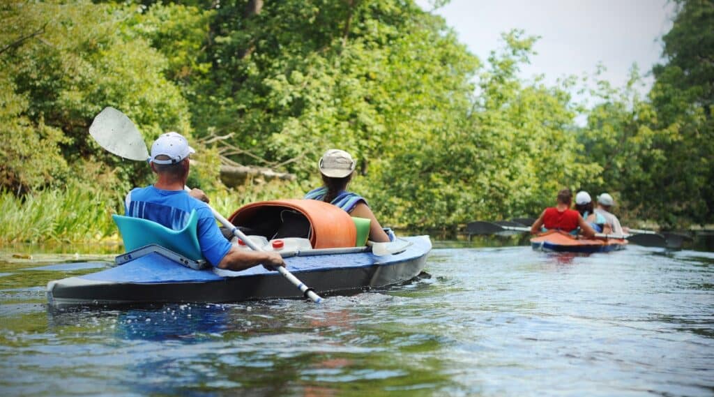 A photograph depicting individuals leisurely floating on a river in a canoe during the summer season. The image captures a serene recreational activity, with people calmly navigating the water in the canoe.