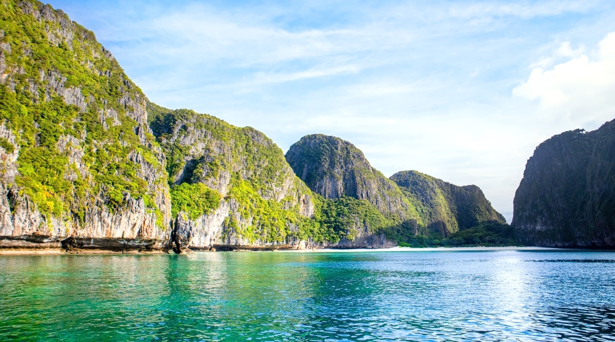 A serene landscape featuring Maya Bay in the Phi Phi Islands, Thailand. The image showcases the picturesque bay, surrounded by lush greenery and crystal-clear waters. The bay is framed by natural rock formations.
