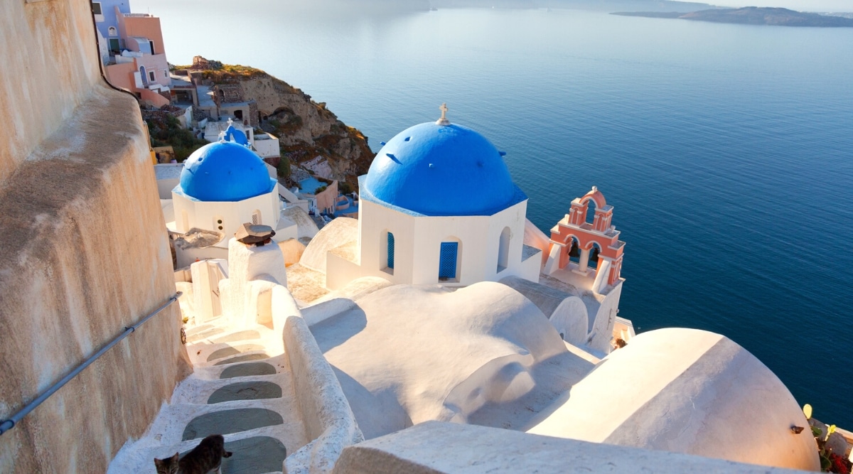 A photograph showcasing Santorini, Greece. The image captures the island's distinct architectural features, including white-washed buildings with blue-domed roofs, against a backdrop of the Aegean Sea. 