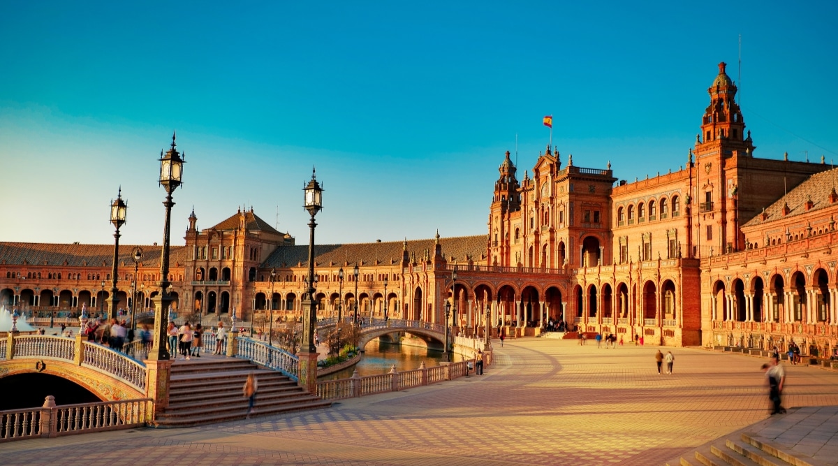 A side view capturing the architectural features of Plaza de Espana in Seville, Spain. The image showcases the square's distinct design within the city center. Architectural elements include arched bridges and detailed balustrades, contributing to the aesthetic appeal of the plaza.