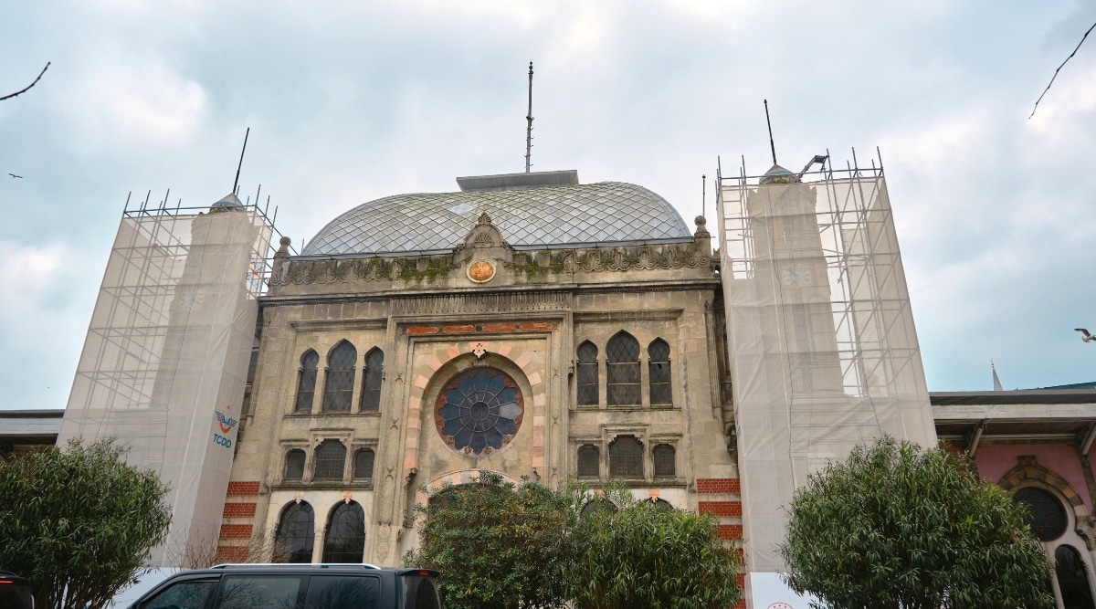 Sirkeci Gar in Istanbul. The structure exhibits a symmetrical facade, adorned with a series of rectangular windows. The use of a neutral color palette, predominantly beige and brown tones.