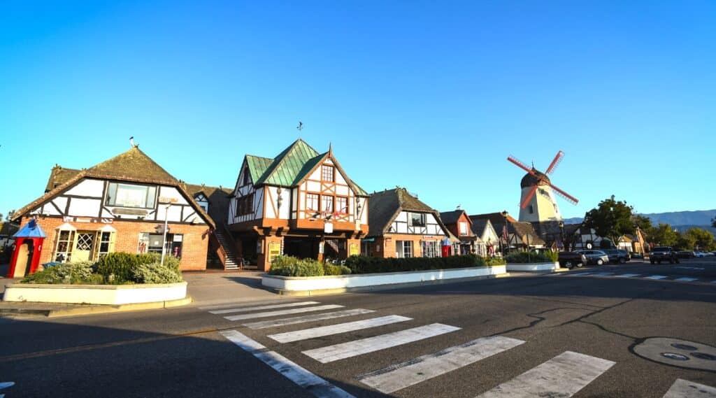 A visual depiction of Alisal Road in the Danish town of Solvang, California. The image showcases the road's architectural and urban characteristics within the context of the town. The street features a series of buildings, likely reflective of the Danish-inspired architecture prevalent in Solvang.