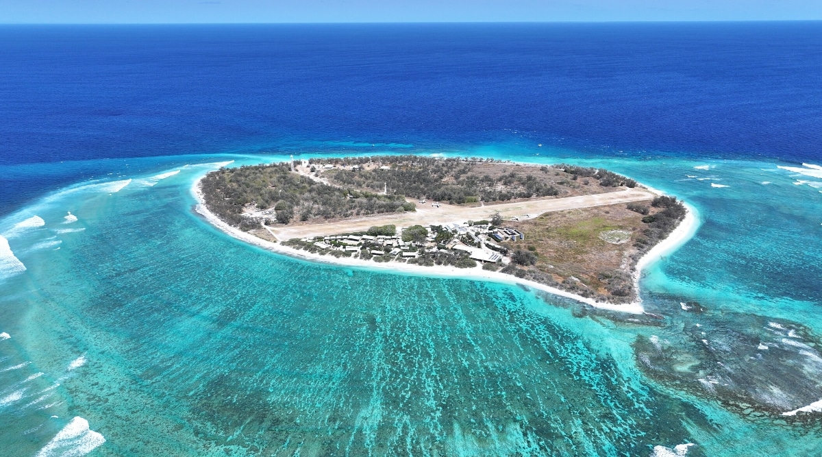 A photograph capturing the remote tropical island destination of Lady Elliot Island within the Great Barrier Reef in Australia. The image features the pristine blue waters surrounding the island, emphasizing its secluded and idyllic setting. The coral reefs and marine ecosystem are subtly visible beneath the water's surface.