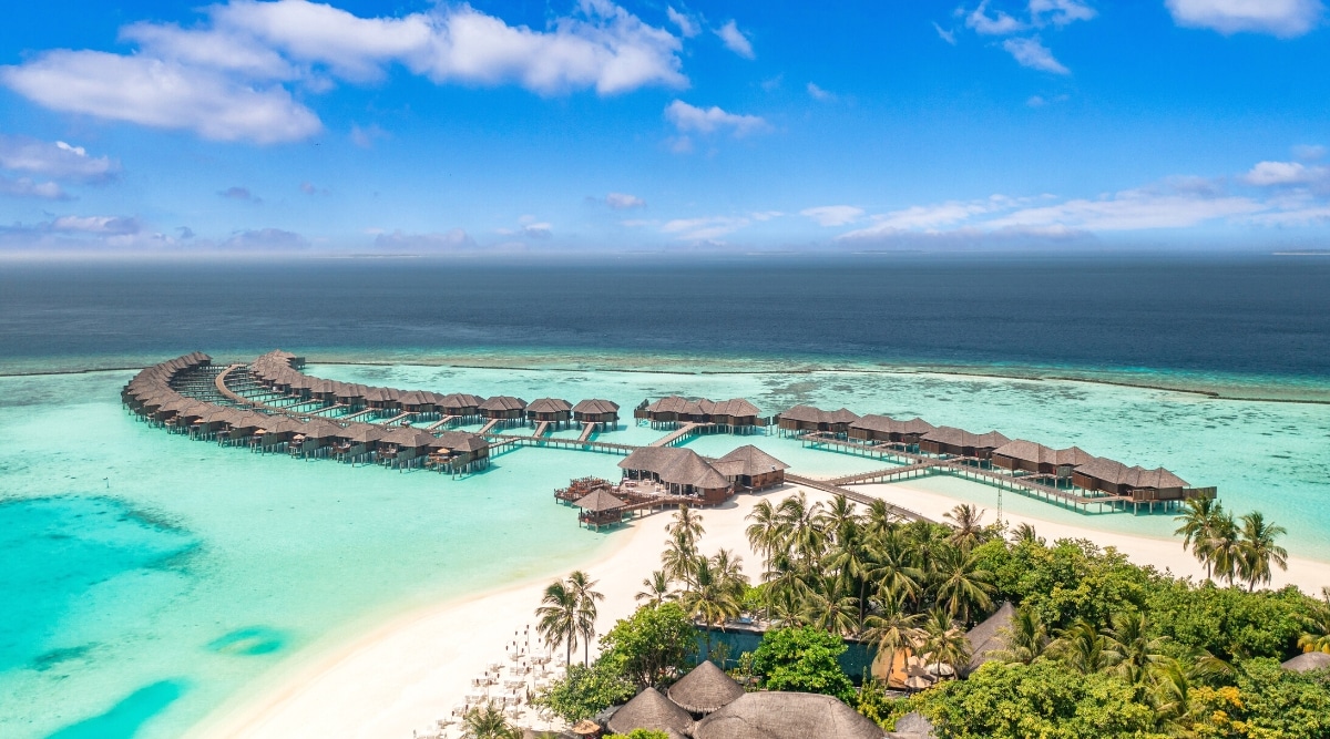 A photograph showcasing The Maldives, an archipelago located in the Indian Ocean. The image captures the characteristic features of the islands, with white sandy beaches, crystal-clear turquoise waters, and overwater bungalows. The weather appears clear and sunny in the depiction.