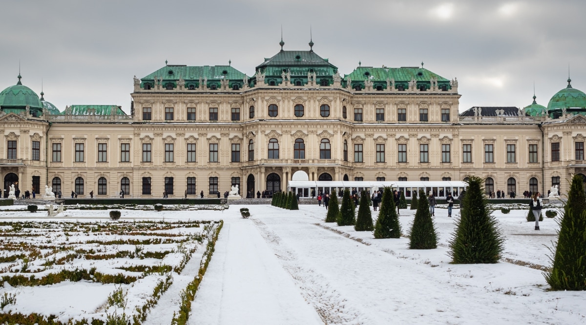 A view of the upper Schloss Belvedere from the palace gardens in Vienna. The image captures the iconic palace against a winter backdrop, with the park blanketed in snow. The architectural features of the Belvedere, including its characteristic facade, are visible in the photograph.