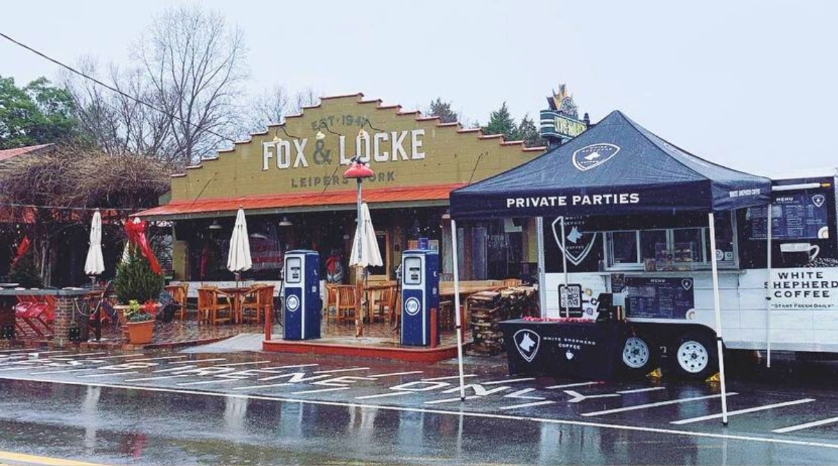 A view of Visit Fox & Locke in Leiper's Fork, Tennessee, captured in a scene devoid of people during a rainy day. The image showcases the exterior of the establishment, and a coffee shop on wheels can be observed nearby.