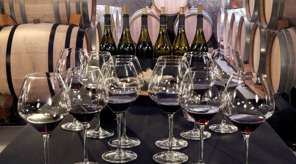 A photograph depicting two filled glasses of wine on a bar counter, surrounded by numerous empty glasses. The image conveys a scene of a bar setting with a focus on the beverages served.
