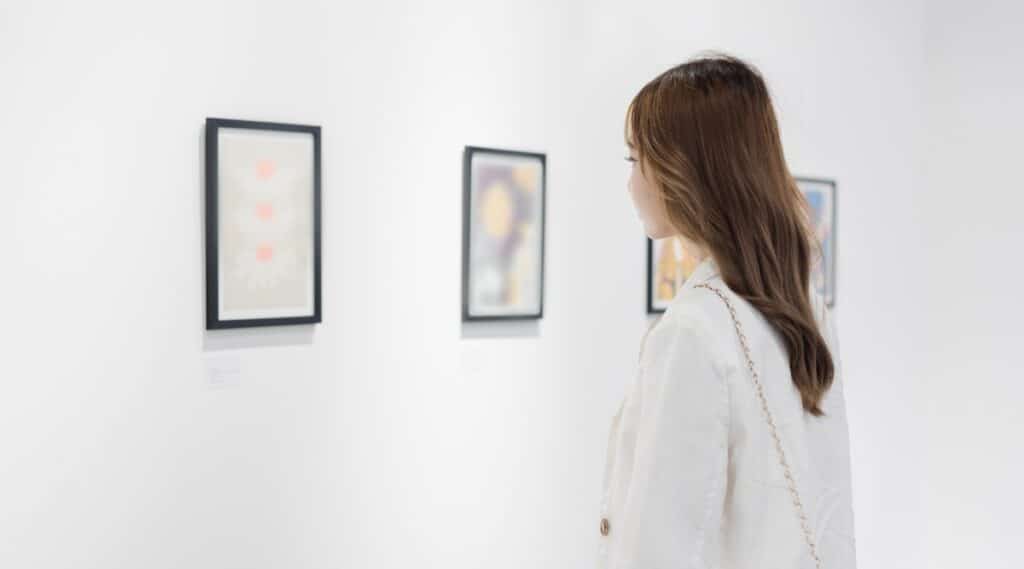The image depicts a woman exploring an art gallery, engaged in observing various pictures on the walls.