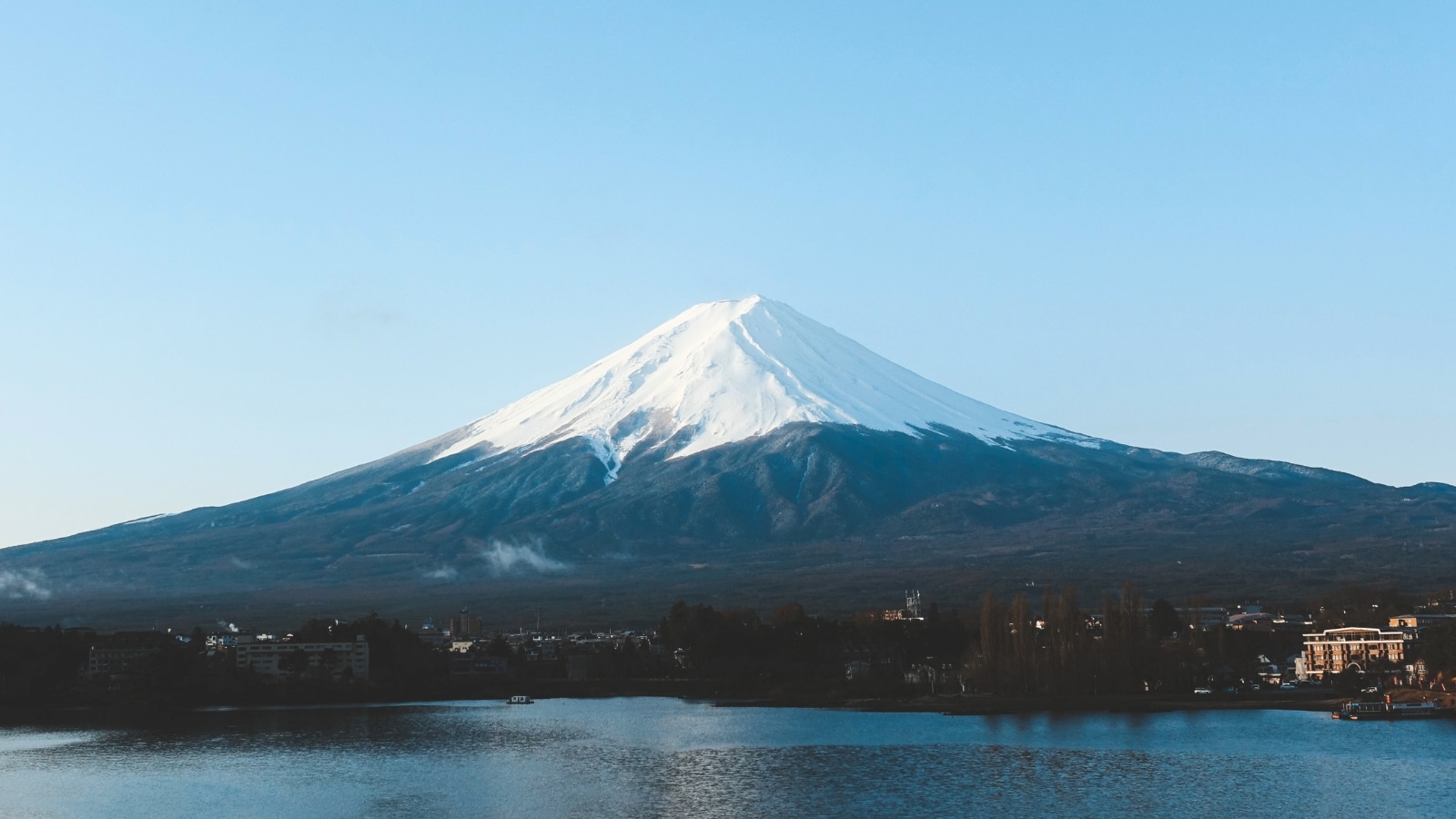 A depiction of Mount Fuji, known as Fujisan, against a clear sky. The image captures the iconic symmetrical cone shape of the mountain, showcasing its prominent presence on the landscape.