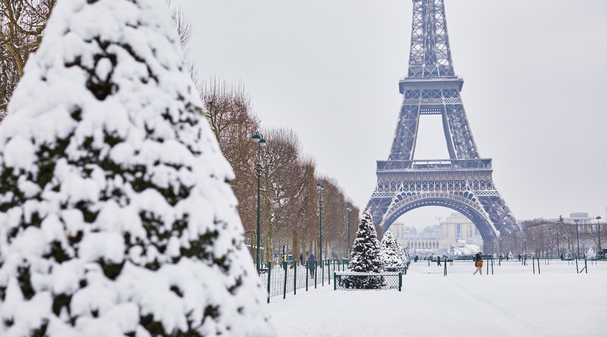 A view of the Eiffel Tower covered in snow, situated in the heart of Paris. The iconic landmark is depicted against a wintry backdrop, with the square below capturing the seasonal conditions. The surroundings are dusted with snow.