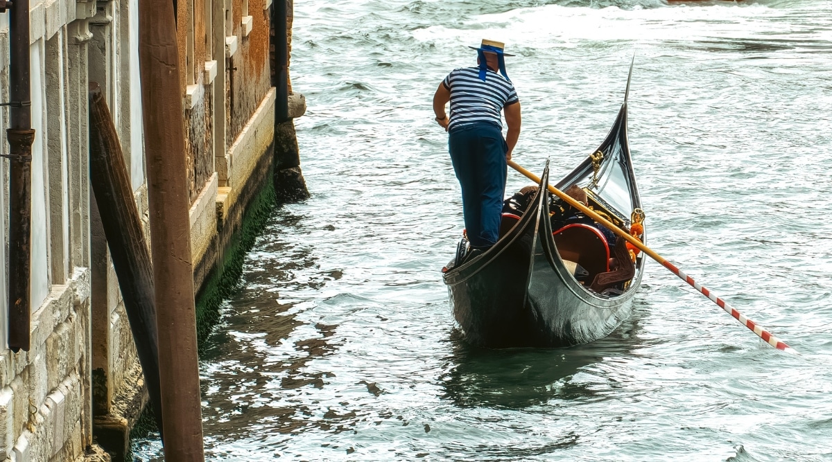 A photograph depicting a man piloting a gondola in Los Angeles, California. The image captures the scene of a gondola moving along a waterway, showcasing the man at the helm.
