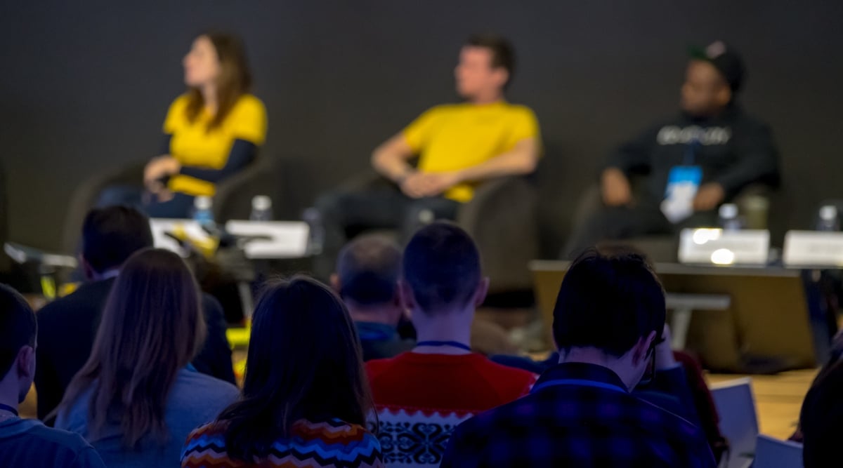 A photograph depicting a blurred scene at the NewFilmmakers Festival in Los Angeles. The image captures attendees in the audience listening to guest speakers on stage.