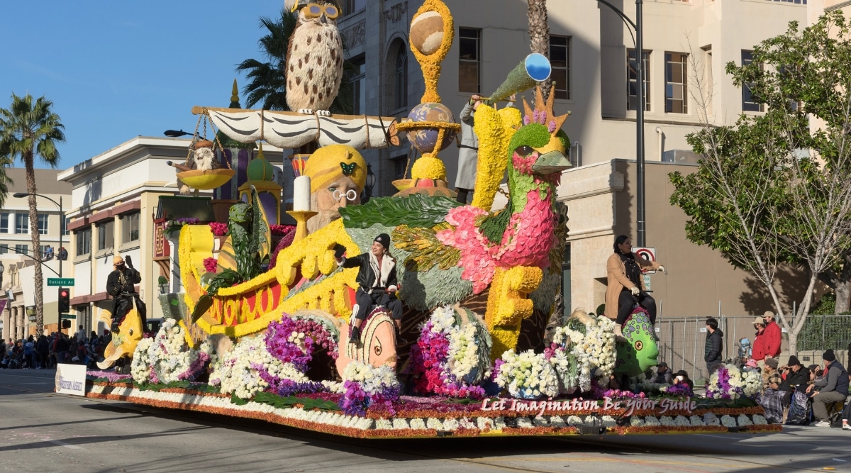 A photograph depicting the Rose Parade in Los Angeles. The image captures the procession of ornately decorated floats moving along a designated route. Participants, adorned in various themed costumes.
