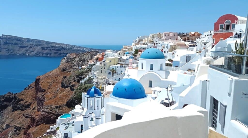 A photograph capturing the picturesque landscape of Santorini, Greece. The image showcases the distinctive white-washed buildings with blue domes, typical of the region's architectural style. Minimalist details include the buildings' stark white exteriors and the traditional blue accents. 