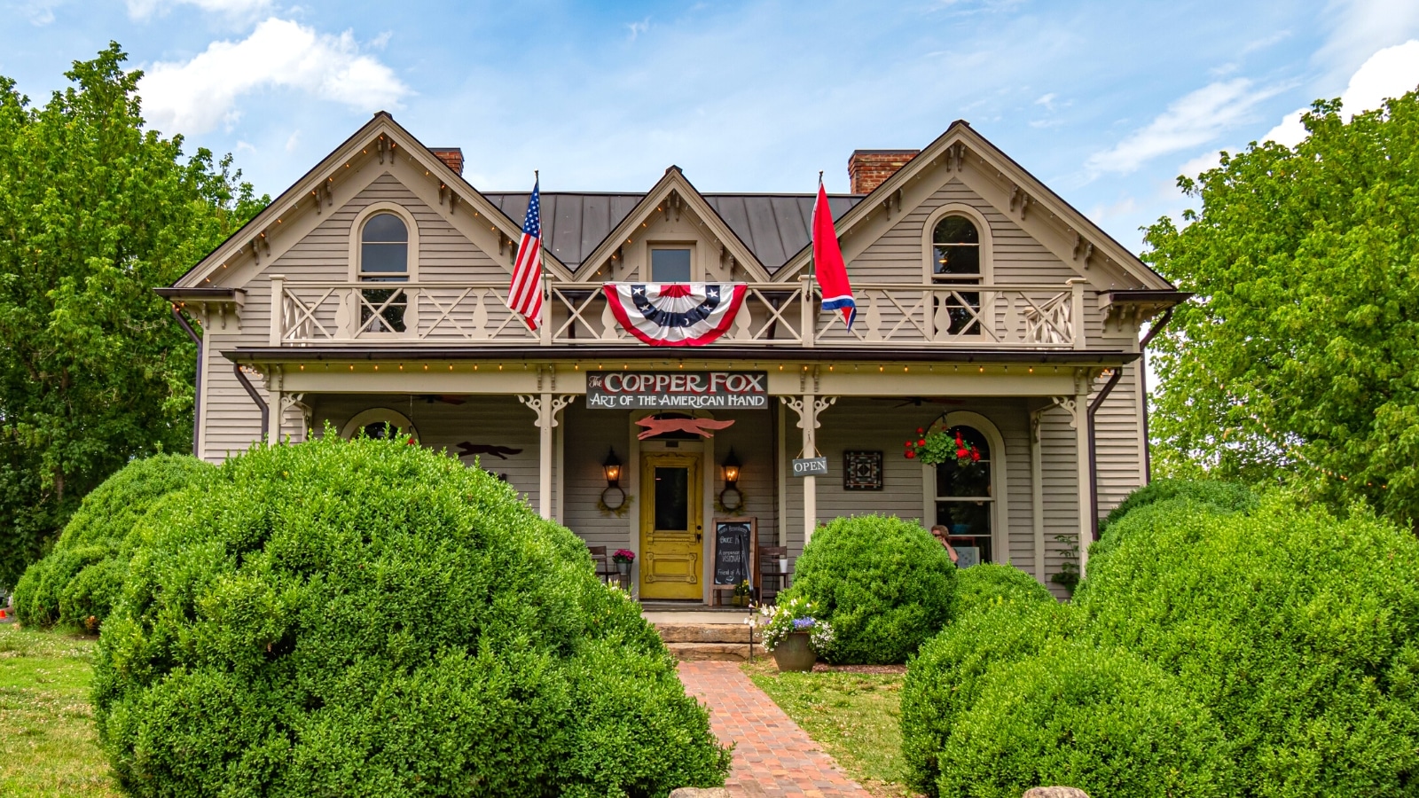 A two-story wooden building in Leipers Fork, Tennessee, presented in grayscale tones. The structure is adorned with two flags: the United States flag and the Tennessee state flag. A stone path in the foreground leads to the building